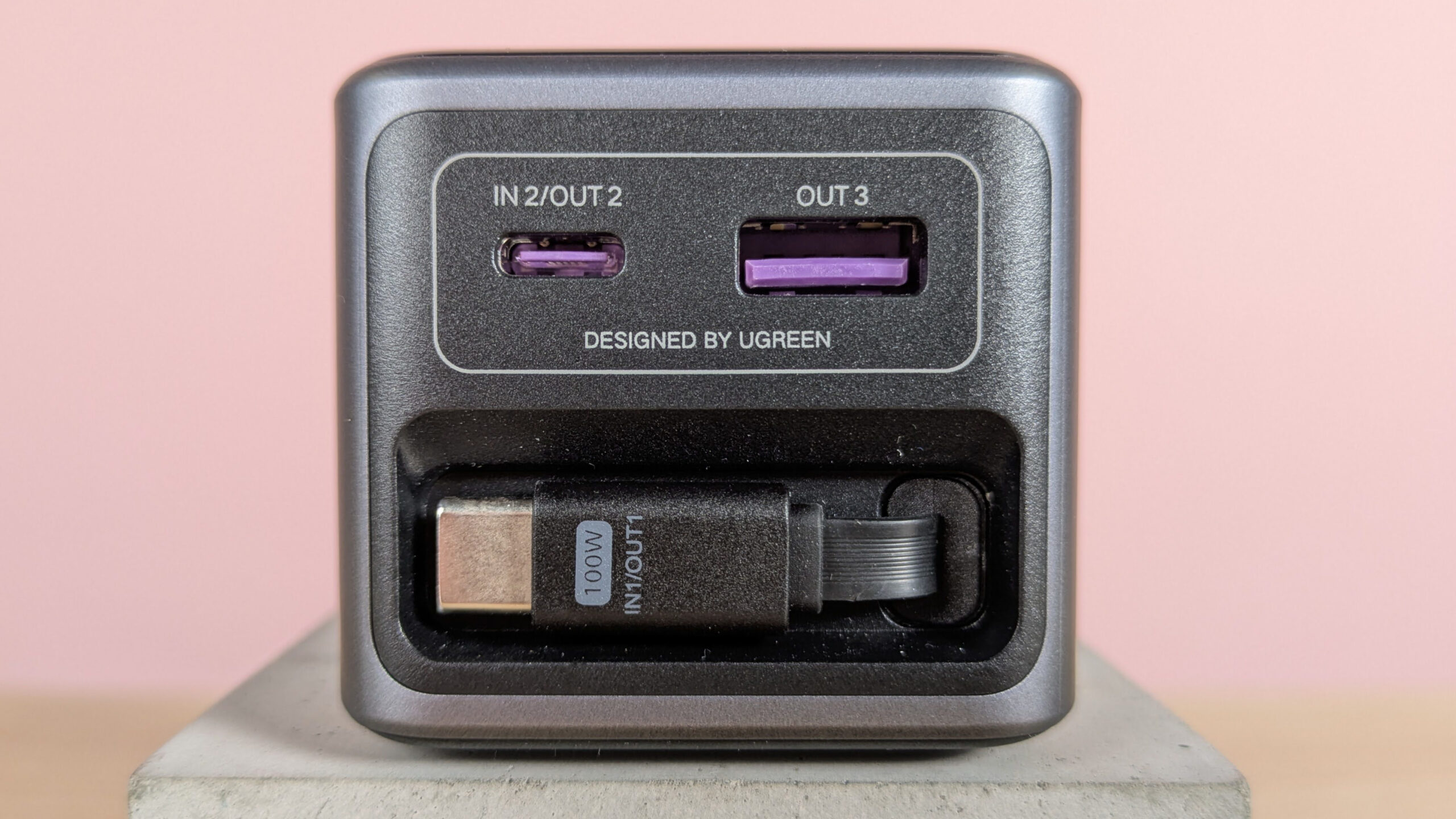 Close-up of ports and retracted USB-C cable on Ugreen Nexode Power Bank 20000mAh 165W, on plinth on desk with pink background